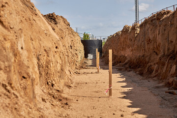 A trench has been prepared for laying water pipes, with wooden stakes to indicate the direction and a concrete well covered with waterproofing mastic