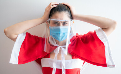 Asian woman in Santy cloth (or Santa Claus) with mask and face shield having stress during covid-19...