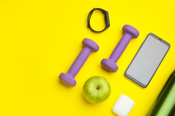 Dumbbells, gadgets and apple on yellow background