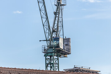 Fototapeta na wymiar Steeple cab of a tower crane above a roof