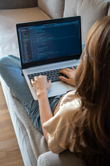 Woman working on a laptop while sitting on the sofa. A girl programmer is coding