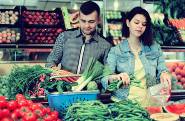 Young loving couple deciding on vegetables in grocery shop