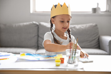 Little girl in paper crown painting with watercolors at home