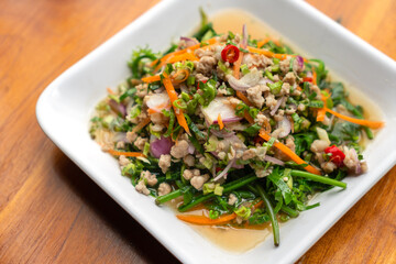 Yum Pak Khut or Diplazium Sour and spicy salad with a combination of chilli, lime, shallot, carrot, herbs, minced pork and some sauce. Healthy Thailand food menu. Close up image food on wooden table.