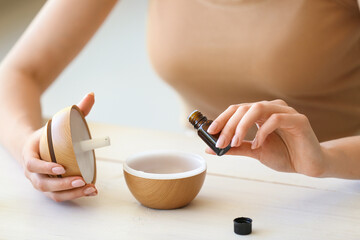 Woman adding essential oil to diffuser on table, closeup