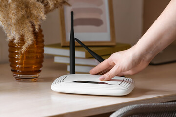 Female hand with wi-fi router on table in room - obrazy, fototapety, plakaty