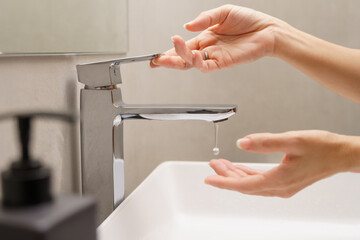 Saving water concept, Close up of beautiful female's hands turning on a faucet with water drop...