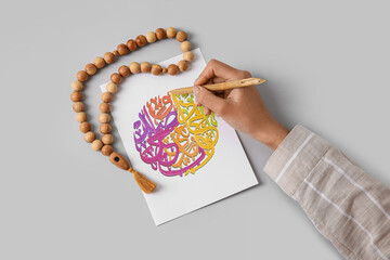 Arabic calligraphist writing on paper sheet against light background
