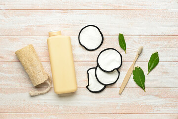 Reusable cotton pads, loofah and bottle with shower gel on light wooden background