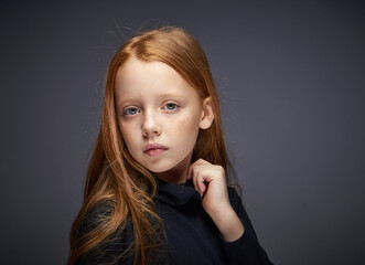 red-haired girl with freckles on her face in a black sweater posing