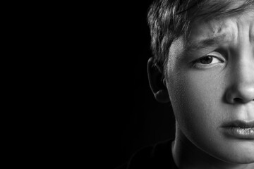 Upset little boy on black background, closeup