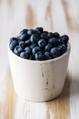 Blueberries in white ceramic bowl on rustic wooden background. Selective focus. Shallow depth of field.
