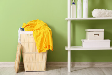 Wooden basket with dirty clothes and shelving unit near green wall