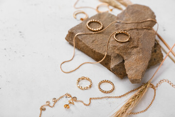 Different golden jewelry, granite stone and wheat ears on grunge background, closeup