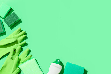 Green cleaning sponges, gloves and bottle of detergent on color background
