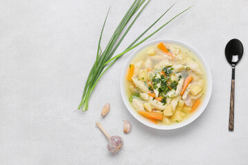 Bowl of tasty dumpling soup, green onion and garlic on light background