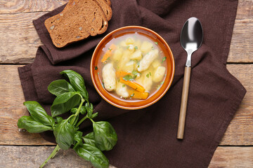 Bowl of tasty dumpling soup, bread and basil on wooden background