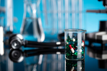 Laboratory investigations concerning test and medicine against covid. Microscope, shethoscope, glass tubes and beakers on blue background.