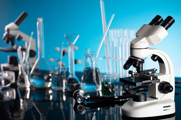 Laboratory investigations concerning test and medicine against covid. Microscope, shethoscope, glass tubes and beakers on blue background.