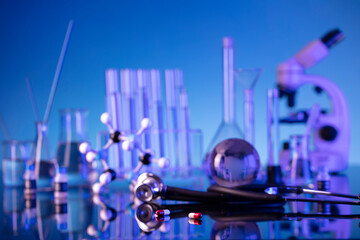 Laboratory investigations concerning test and medicine against covid. Microscope, shethoscope, glass tubes and beakers on blue background.