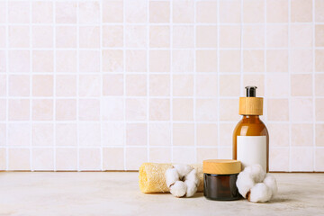 Fototapeta na wymiar Cosmetic products, sponge and cotton flowers on table against tile wall