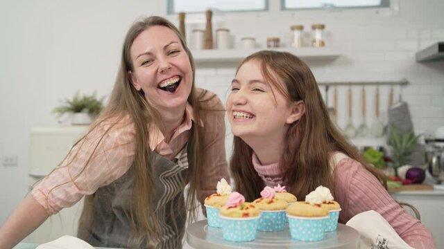 Playful daughter teasing mother putting cherry in her mouth while baking bakery in the kitchen.
