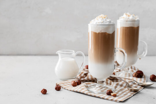 Glass cups of tasty latte and jug with milk on white background