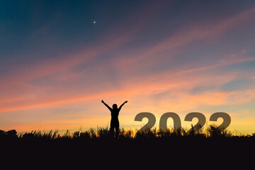Stepping into 2022 with confidence to be successful, silhouette of a young woman raising her hand in the sunset sky