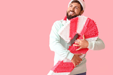 Handsome man in Santa hat with candy cane pinata on pink background