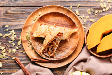 Plate with pieces of tasty pumpkin strudel on wooden background