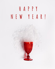 Red festive wine glass from which snow scattered, creative concept of winter holidays, Christmas party. Colored glassware trend wine glass and text happy new year