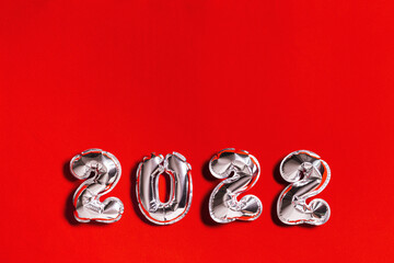 Silver balloons number 2022 New Year on red cloth background with copy space Layout for greeting card or invitation for new year party