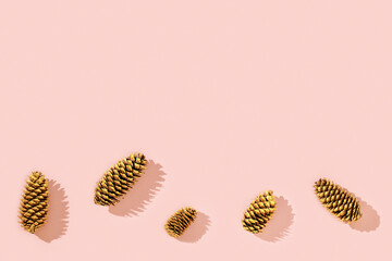 Christmas decorations from natural pine cone painted golden colored on pink. Trendy winter holiday background