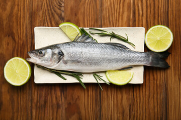 Board with fresh uncooked sea bass fish and lemon on wooden background