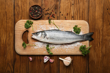 Board with fresh uncooked sea bass fish on wooden background