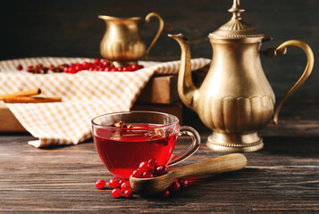 Cup of tasty lingonberry tea and spoon with berries on wooden background