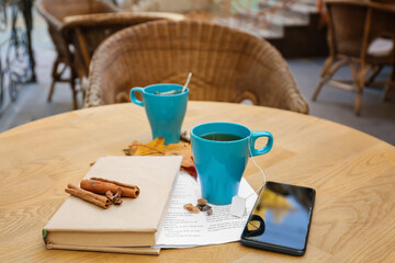 Blue cup of hot tea with book and mobile phone on table in cafe