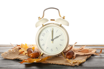 Alarm clock, acorns and autumn leaves on table against white background. Daylight saving time end