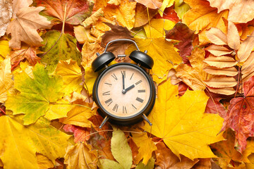 Alarm clock on autumn leaves. Daylight saving time end