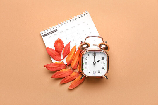 Alarm clock, calendar and autumn leaves on color background. Daylight saving time end