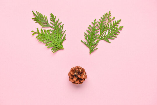 Creative composition with reindeer face made of fir branches and pine cone on pink background
