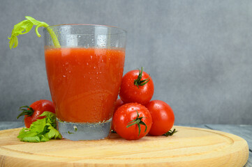 A glass of tomato juice, tomatoes, parsley leaves on a cutting board