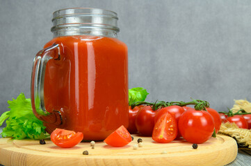 A jar of tomato juice, tomatoes, parsley leaves, allspice on a cutting board