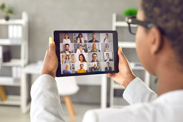 Manager having virtual meeting with team of diverse colleagues. View over shoulder monitor display of modern digital tablet gadget. International online business communication, remote teamwork concept