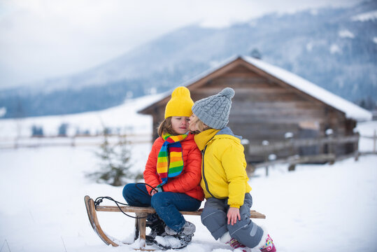 Children kissing. Happy little children and sledding in winter. Kids kiss on snow slides in winter. Son and daughter enjoy a sleigh ride.