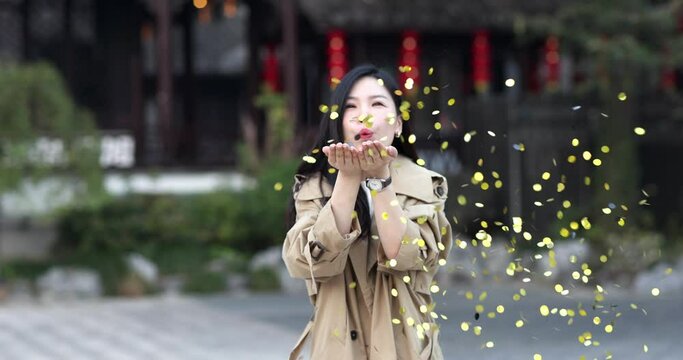 Lifestyle Portrait of young asian woman with brunette hair blowing golden confetti outdoor. Person celebrating birthday, Chinese new year 2022 or national holiday October 1th. Slow motion