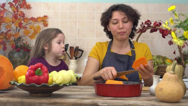 Happy daughter is helping mother to prepare traditional festive pumpkin pie for Thanksgiving dinner. American family celebrates Thanksgiving. A Girl Learns to Bake. Fall home decor