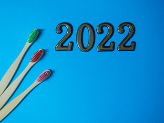 2022 and dental concept. Close up view of photo with 2022 and three wooden colorful toothbrush on blue background with copy space for text. Christmas medical card. Merry Christmas and Happy New Year.