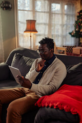 Black man relaxing on sofa and using digital tablet