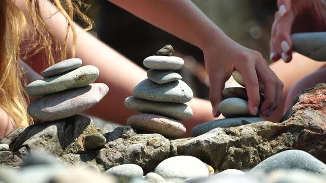Woman bilds stones pyramid on the seashore on a sunny day on the blue sea background. Happy holidays. Pebble beach, calm sea, travel destination. Concept of happy vacation on the sea, meditation, spa